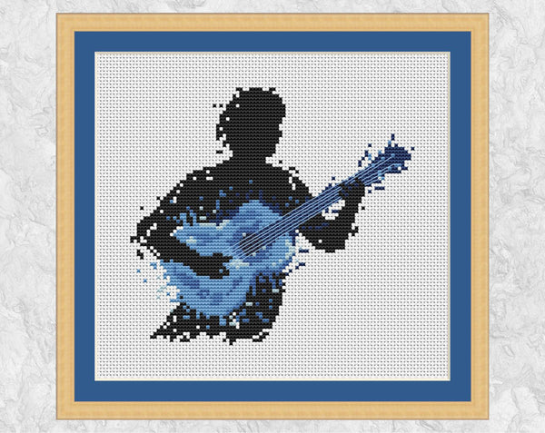 Male guitarist music cross stitch pattern - splattered paint style. Shown with frame.
