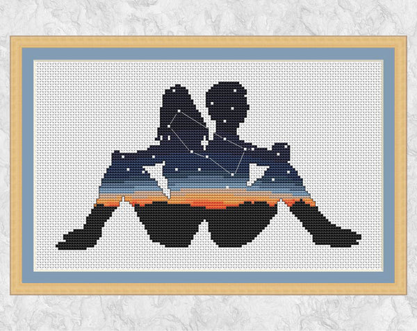 Zodiac cross stitch pattern of the twins of Gemini sitting back to back, filled with a scene of the constellation Gemini against the last of the setting sun. Shown with frame.