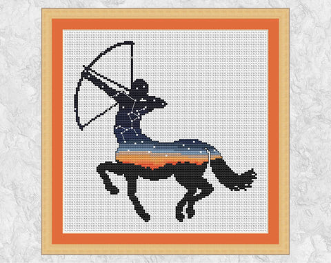 Cross stitch pattern of the silhouette of a centaur about to shoot an arrow, filled with a sunset and night sky showing the constellation of Sagittarius. Shown with frame.