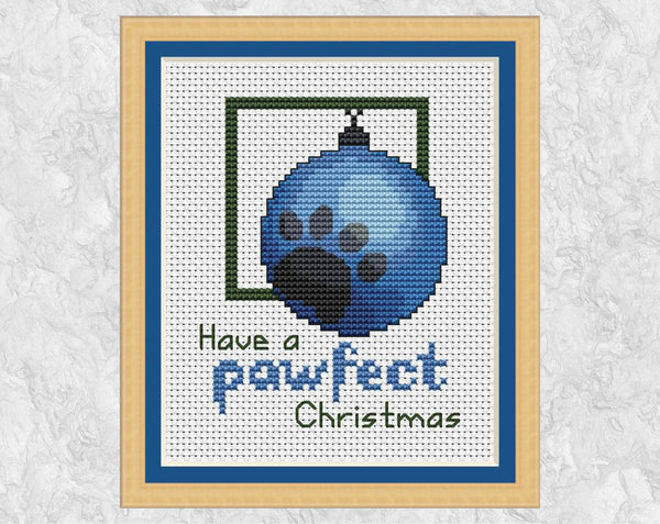 Cross stitch pattern of a blue bauble with a grey paw print on it, with the words 'Have a pawfect Christmas'. Shown with frame.
