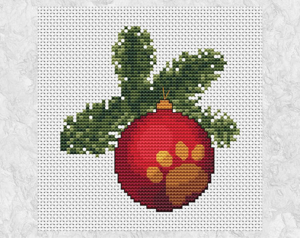 Cross stitch pattern of a bauble engraved with a paw print hanging from a Christmas tree branch. Shown without frame.