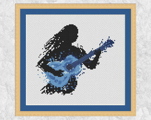 Female guitarist music cross stitch pattern - splattered paint style. Shown with frame.