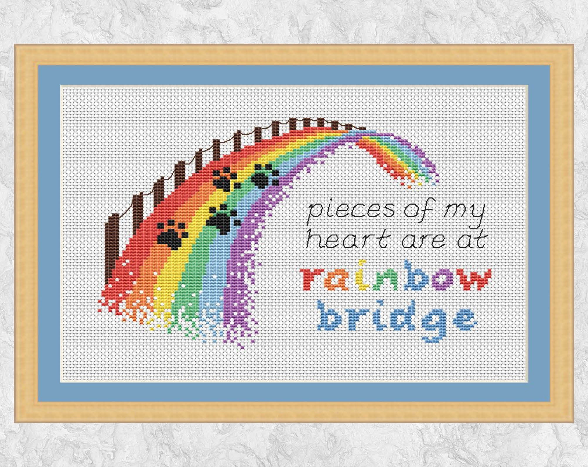 Cross stitch pattern of a rainbow bridge with the quote "pieces of my heart are at rainbow bridge". Shown with frame.
