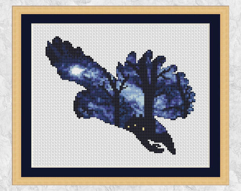 Cross stitch pattern of the silhouette of a swooping owl, filled with a scene of a woodland illuminated by moonlight, with a cottage nestled amongst the trees. Shown with frame.