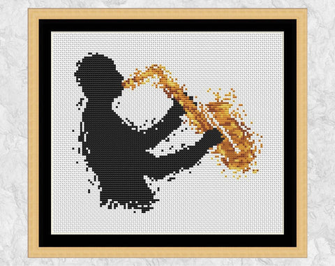 Cross stitch pattern of splattered paint male saxophone player. Shown with frame.