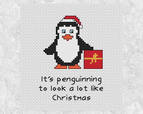'It's Penguinning to Look a Lot Like Christmas' cross stitch pattern with penguin wearing Santa hat and holding present. Shown without frame.