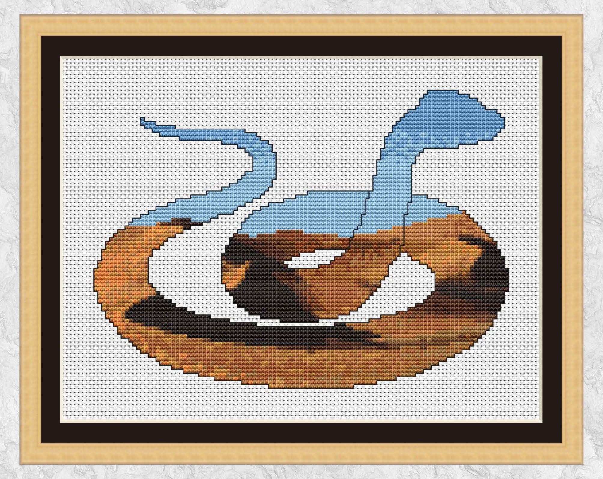 Cross stitch pattern PDF of the silhouette of a snake, filled with a desert of shifting dunes. Shown with frame.