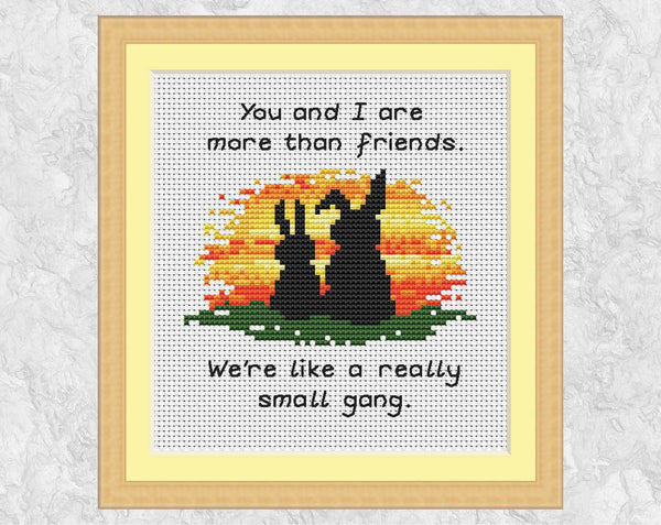 Cross stitch pattern of two bunny rabbits watching a sunset with the words 'You and I are more than friends. We're like a really small gang.' Shown in frame.