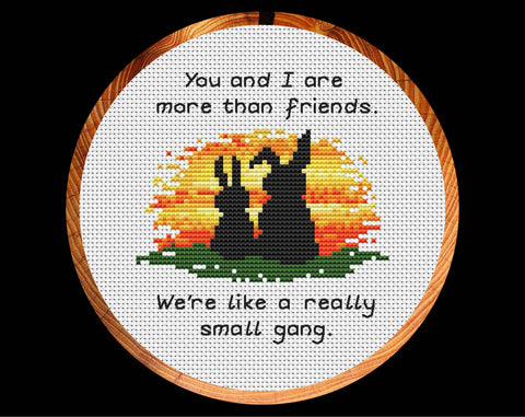 Cross stitch pattern of two bunny rabbits watching a sunset with the words 'You and I are more than friends. We're like a really small gang.' Shown in hoop.