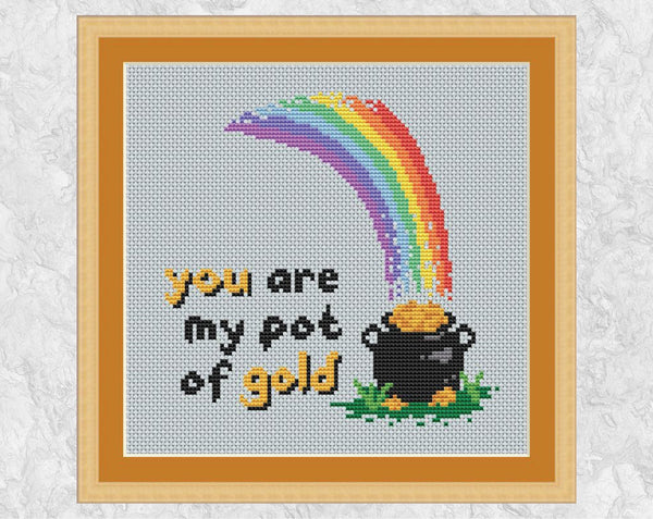 Cross stitch pattern of a rainbow falling on a pot of gold, with the words 'you are my pot of gold'. Shown in frame.