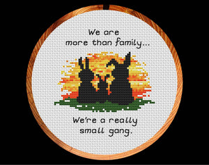 Cross stitch pattern of three bunny silhouettes against a sunset, with the words "We are more than family... We're a really small gang.". Shown in hoop.