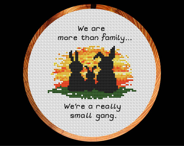 Cross stitch pattern of three bunny silhouettes against a sunset, with the words "We are more than family... We're a really small gang.". Shown in hoop.