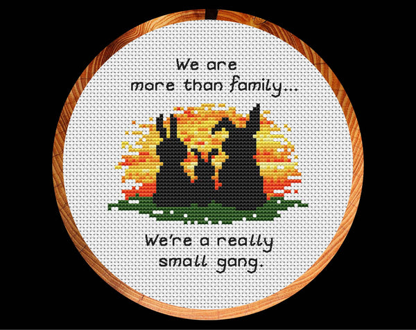 Cross stitch pattern of three bunny silhouettes against a sunset, with the words "We are more than family... We're a really small gang.". Shown in hoop.