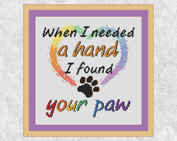 Cross stitch pattern PDF of the words "When I needed a hand I found your paw", with a heart and paw print. Shown with frame.