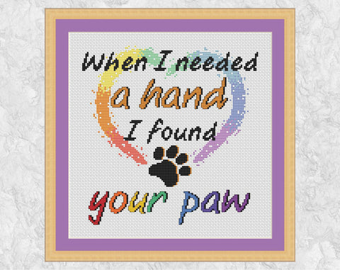 Cross stitch pattern PDF of the words "When I needed a hand I found your paw", with a heart and paw print. Shown with frame.