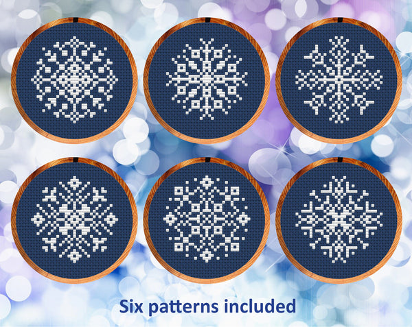 Six mini snowflake cross stitch patterns in white on dark blue fabric