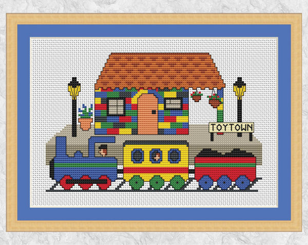 Toy Train and Station cross stitch pattern - cartoon train arriving at Toytown Station, made of colourful toy bricks. Shown with frame.
